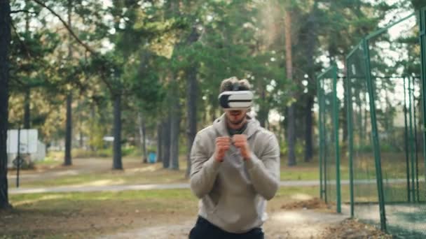 El joven con gafas de realidad virtual está ejercitándose en el boxeo del parque solo con auriculares y brazos en movimiento como si estuviera peleando. Gadgets modernos, gente y concepto de la naturaleza . — Vídeos de Stock