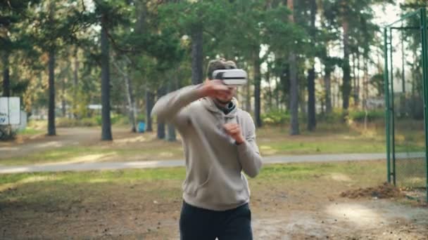 El tipo activo lleva gafas de realidad aumentada y boxeo disfrutando de la simulación de lucha en gadget durante el entrenamiento en el parque. Concepto de juventud, deporte y diversión . — Vídeos de Stock