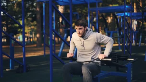 Beau barbu gars travaille à l'extérieur en utilisant une machine de musculation dans l'aire de loisirs du parc de la ville le jour de l'été. Concept de personnes, de musculation et de sport . — Video