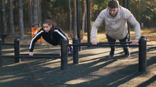 Αρσενικά και θηλυκά φοιτητών άσκηση σε εξωτερικούς χώρους μαζί κάνει pushups σε χαμηλή οριζόντια γραμμή κατάρτισης μυς του βραχίονα και του στήθους. Άνθρωποι και προπόνηση έννοια. — Αρχείο Βίντεο