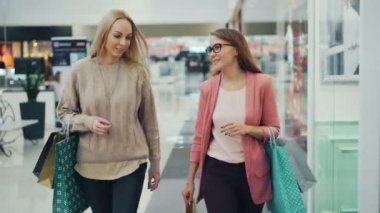 Neşeli kadın konuşmak ve birlikte kağıt torba taşıyan biz çarşıda yürürken el hareketi. Kız trendy giyim ve aksesuarları giyiyor.