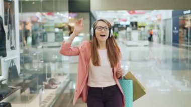 Kaygısız genç bayan öğrenci kulaklık üzerinden müzik, dans ve alışveriş merkezinde hafta sonu, Satınalmalar ve modern teknoloji zevk şarkı.