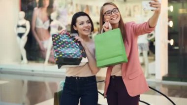 Mutlu shopaholics kağıt torbalar alışveriş mermiyi tutuyor ve poz, gülen ve having fun smartphone kamera ile ile selfie alıyor. Gençlik yaşam tarzı kavramı.