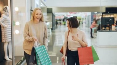 İyi görünümlü kız öğrenci yürüme alışveriş merkezinde eğleniyor birlikte sohbet ve holding gülüyor kağıt çanta. Satılık, insanlar ve shopaholism kavramı.