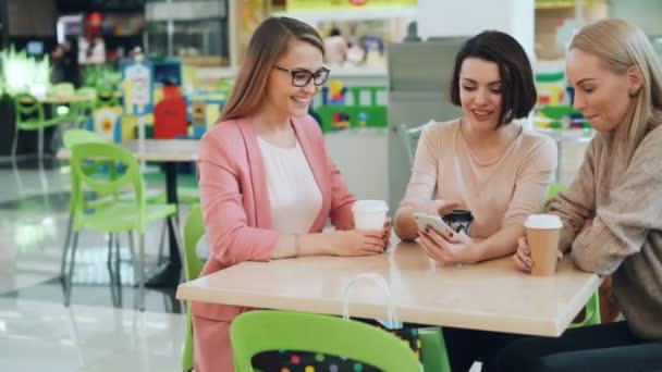 Beaux étudiants utilisent smartphone assis dans un café ensemble et regardant l'écran puis faire haute-cinq et rire. La jeunesse moderne, gadgets et concept d'amitié . — Video