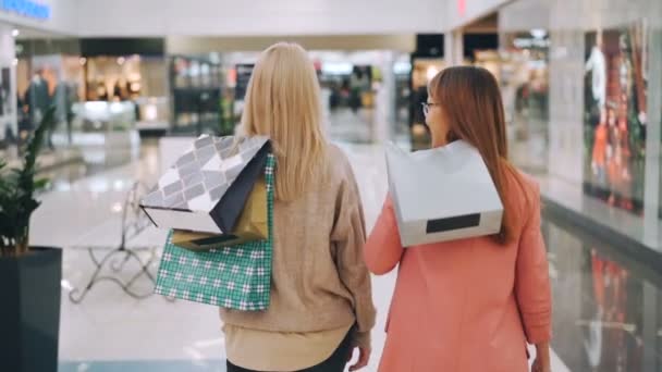 明るい保持しているショッピング モールで一緒に歩いている幸せな若い女性友人のスローモーション バッグ、カメラに転換し、笑みを浮かべてします。ショッピングやお店のコンセプト. — ストック動画