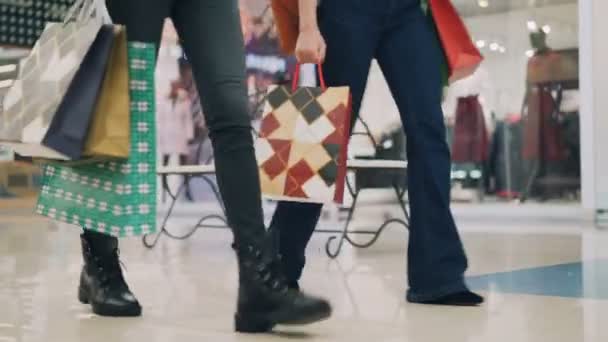 低角度拍摄的苗条的女孩穿着牛仔裤走在商场一起携带五颜六色的纸袋后, 购买一天。购物狂、青年和商店概念. — 图库视频影像