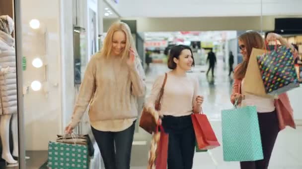 Amigos meninas bonitas estão se divertindo no shopping dançando e girando com sacos de papel, sorrindo e rindo apreciando compras e tempo livre . — Vídeo de Stock