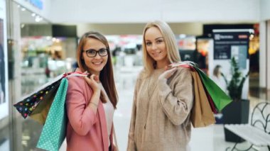 Güzel kızlar kameraya bakıyor ve gülümsüyor büyük mağazada alışveriş torbaları tutan portresi. Genç kadın trendy kıyafetler ve aksesuarlar üzerinde var.