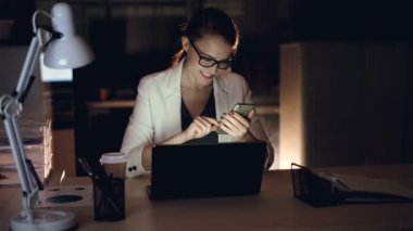 Yakışıklı sarışın smartphone manifatura kullanma ve office gece geç saatlerde yalnız oturan gülümsüyor. Modern araçlar, çalışkan Gençlik ve iletişim kavramı.