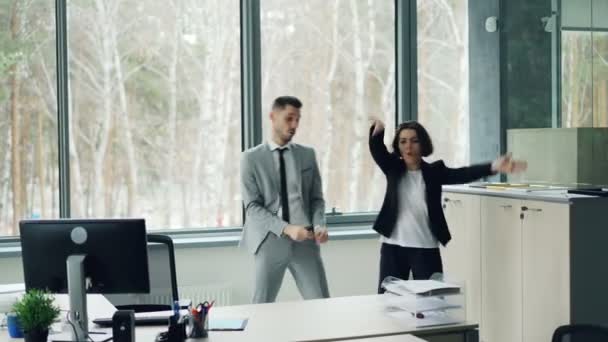 Красива бізнес-леді вчить свого колегу-чоловіка танцювати, слухати музику і рухатися в офісі, насолоджуючись відпочинком від роботи. Люди в костюмах . — стокове відео