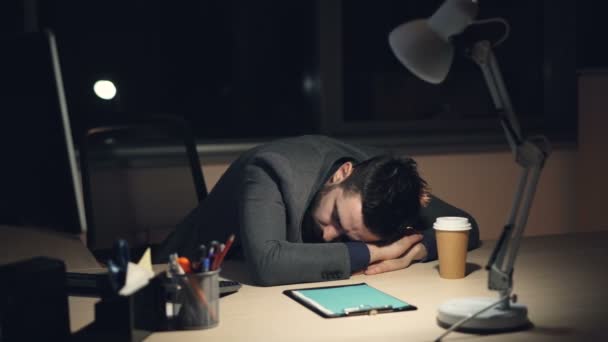 Cansado de terno dormindo na mesa de trabalho no escritório tarde da noite depois do dia de trabalho ocupado. Computador ligado, café takeaway e lâmpada são visíveis na mesa . — Vídeo de Stock