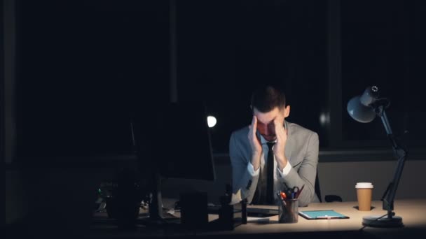 Αργά τη νύχτα κάθεται σε δουλειά γραφείου μόνο φινίρισμα τρίβοντας το πρόσωπό του έχοντας πονοκέφαλος κουρασμένος νεαρός άνδρας στο κοστούμι λειτουργεί στον υπολογιστή. Έννοια υπερκόπωση και της νεολαίας. — Αρχείο Βίντεο