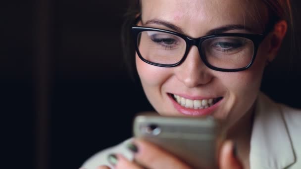 Primer plano de chica guapa usando gafas usando la pantalla táctil del teléfono inteligente y sonriendo disfrutando de la comunicación. Tecnología moderna y concepto juvenil . — Vídeos de Stock