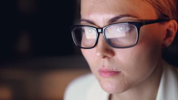 Primer plano de la hermosa mujer joven con gafas usando la computadora trabajando hasta tarde en la noche en la habitación oscura de la oficina. Empresarios, concepto de trabajo y juventud . — Vídeo de stock