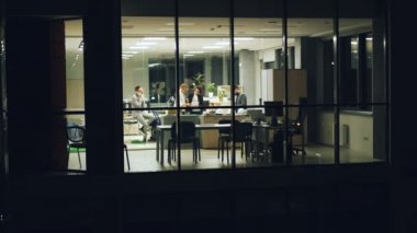 Grup insanlar iş takımının üstünde hareket eden telefon, iş tartışmak ve belgeleri seyir konuşurken gece geç ofiste çalışıyoruz. Panoramik penceresinden dışarı--dan görünüm.