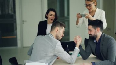 Erkek ofis işçi yaşıyorsanız eğlenceli kızlar smartphone kullanarak ve çocuklar tezahürat Yarışması kaydederken arm-wrestling yapıyor. İş sonu ve gençlik kavramı.