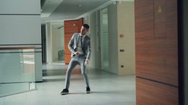 Sakallı yakışıklı çalışan resmi kıyafeti içinde yalnız kollar, bacaklar ve vücut hareketli ofis merkezi lobisinde dans ediyor. Sevinç ve olumlu duygular kavramı.