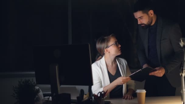 Elfoglalt fiatalok férfi és női kollégák irodában dolgoznak éjjel beszél, és a számítógép képernyője. A srác tartja a dokumentumok mappa. — Stock videók