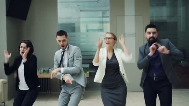 Szczęśliwy zespół mężczyzn i kobiet w partii pracy razem tańczyć ciał poruszających, śmiejąc się i śpiewając, zrelaksować się w sali. Koncepcja współpracowników, relaks i emocje. — Wideo stockowe