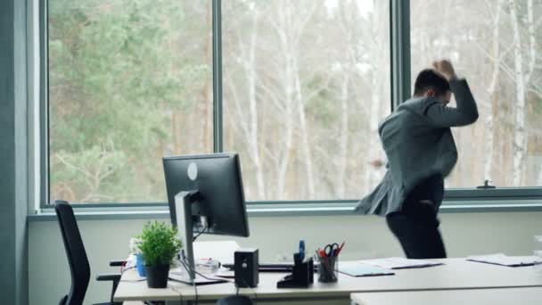 El hombre de negocios barbudo expresa emociones positivas bailando, quitándose la chaqueta y tirando papeles desde el escritorio divirtiéndose en una bonita sala de oficina . — Vídeo de stock