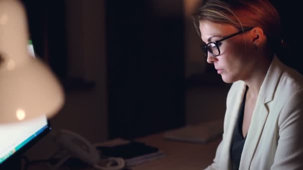 Tilt dolů záběr hezké mladé ženy pracující na počítači pozdě v noci psaní pomocí klávesnice sedí u stolu sám. Přesčasová práce a kariéra koncepce. — Stock video