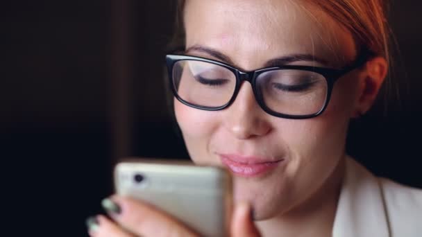 Fejlövés a csinos, fiatal hölgy szemüveget használ smartphone képernyő szemöldök, szörfözés az interneten, és mosolyogva megérintésével. Modern gadgets és ifjúsági koncepció. — Stock videók