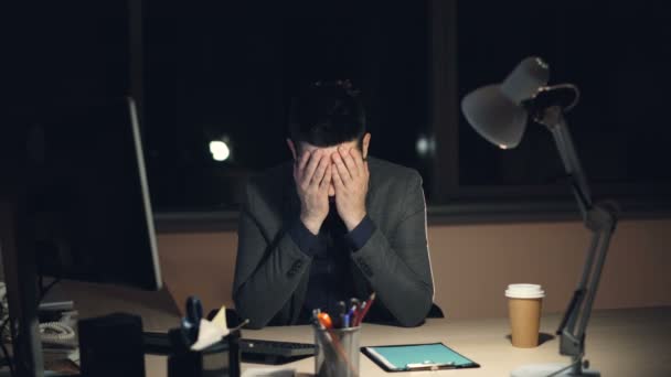 Joven cansado en traje y corbata está trabajando en la computadora en la oficina por la noche sentado en el escritorio en el cuarto oscuro, mirando la pantalla y escribiendo. Trabajo duro y concepto de estrés . — Vídeo de stock