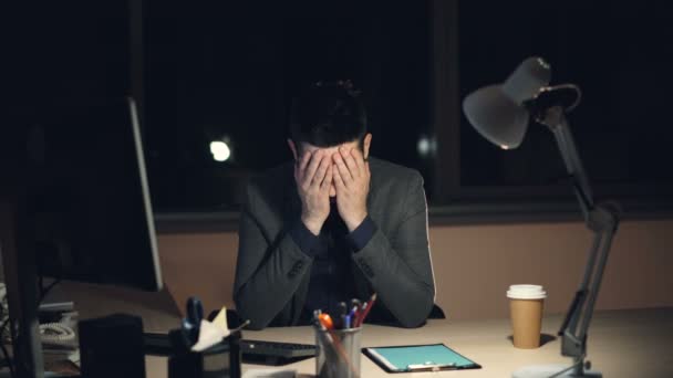 Tired young man in suit and tie is working on computer in office at night sitting at desk in dark room, looking at screen and typing. Hard work and stress concept. — Stock Video