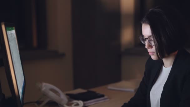 ハンサムな若いブルネットは自信未完のプロジェクトに焦点を当てた夜オフィスのコンピューターに取り組んでいる彼女の仕事に専念。若さと技術の概念. — ストック動画