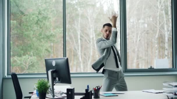 Carefree guy in formalwear is dancing at work alone moving body and throwing papers from desk expressing excitement and happiness then walking away. — Stock Video