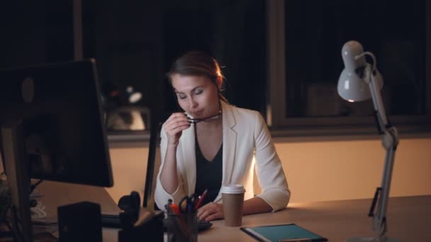 Bionda stanca in occhiali e tuta sta lavorando sul computer a tarda notte e beve caffè da asporto sensazione di stanchezza ed esaurimento. Lavoro, superlavoro e bevande concetto . — Video Stock