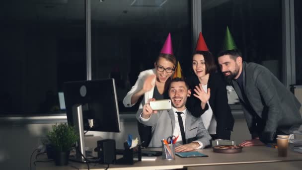 Group of young people is making online video call skyping from office wearing party hats talking, waving hand, sending air kisses and showing thumbs-up. — Stock Video