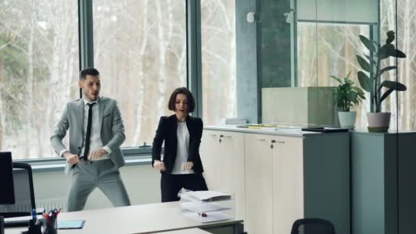 Vrolijke paar collega's is dansen in kantoor plezier samen bewegende armen en het lichaam ontspannen na het werk. Millennials, levensstijl en vreugde jeugdconcept. — Stockvideo