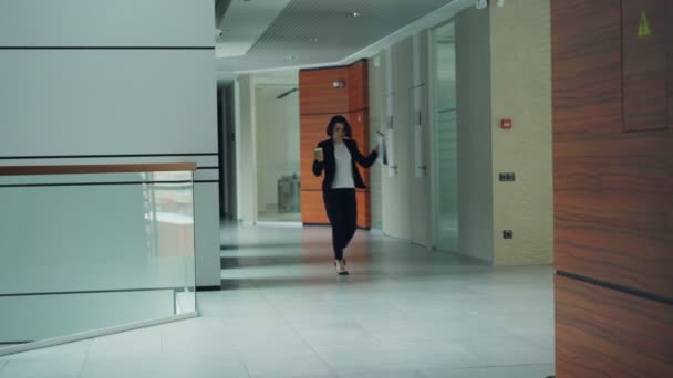 Emotionele jongedame zakenvrouw is dansen in zaal van business center holding documenten en en-klare koffie genieten van vrijheid tijdens lunchpauze. Baan en leuk concept. — Stockvideo