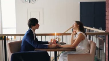 Mutlu çift genç adam ve kadın birlikte tarihte restoranda oturan eller tutarak konuşuyoruz. İnsanlar güzel giyim elbise giyiyor ve elbise.