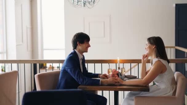Jóképű fickó beszél barátnőjével időpontban ül az asztalnál együtt, és nevetve élvezi romantikus pillanat és beszélgetés. Emberek és érzések koncepció. — Stock videók