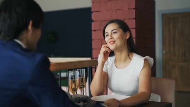 Giovane donna allegra in costume sta parlando con il suo ragazzo in data seduta a tavola insieme tenendosi per mano. Persone romantiche, incontri e concetto di relazione . — Video Stock