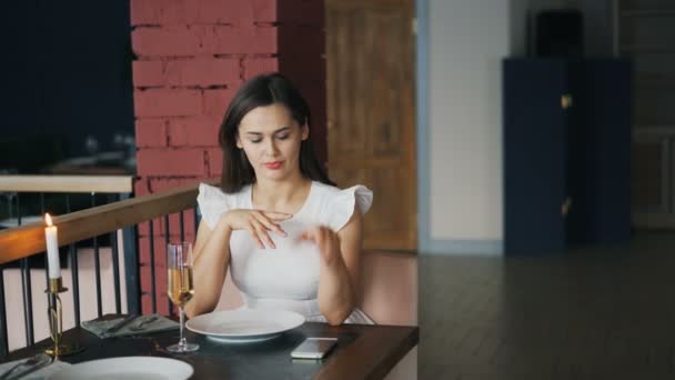 Attraktiv ung kvinna i vacker klänning väntar på sin pojkvän i restaurangen sitter vid bordet ensam och använda smartphone kontroll tid. Dating och teknik koncept. — Stockvideo