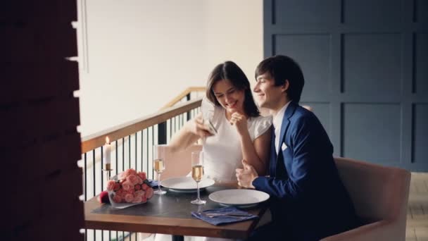 Gente feliz hombre y mujer se están tomando selfie con la cámara del teléfono inteligente en el restaurante besando y riendo y luego viendo fotos y hablando. Concepto de autorretrato y amor . — Vídeos de Stock