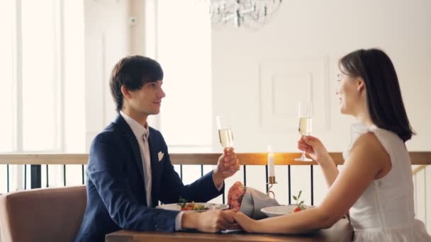 Dziewczyna i chłopak są rozmowy, brzęk okulary i pić szampana na romantyczną randkę w wytwornej restauracji. Romans, miłość i dobrze koncepcja gastronomiczna — Wideo stockowe