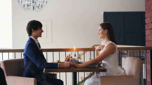 Restoranda evlenme teklifi sırasında mutlu çift yan görünüm, adamın konuşuyor ve nişan yüzüğü kızlar parmağında koyarak, genç kadın gülüyor ve Evet diyerek. — Stok video