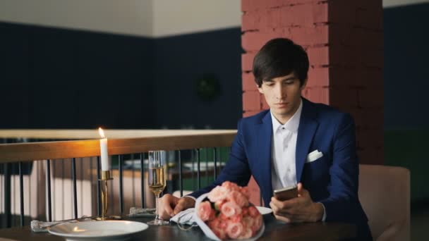 Goed geklede boze jonge man wacht op zijn late vriendin in het restaurant, met behulp van smartphone dan verlaten. Moderne technologie en ongelukkig mensen concept. — Stockvideo