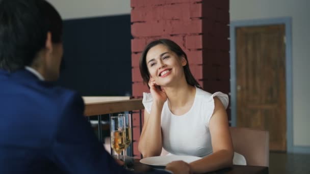 Jovem feliz em vestido bonito está falando com seu namorado na data sentado à mesa juntos de mãos dadas. Juventude romântica, namoro e conceito de relacionamento . — Vídeo de Stock