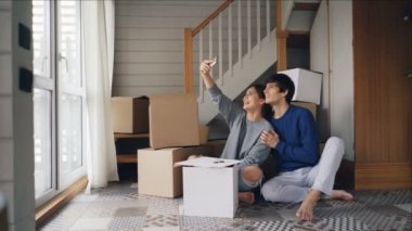Mutlu çift yeni daire satın aldıktan sonra selfie alıyor. Genç insanlar poz ve arka planda kutuları ile smartphone kamera bakarak öpüşme.