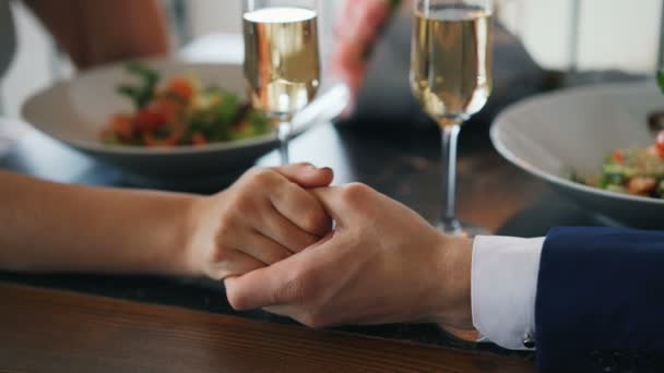 Primer plano de la mano masculina sosteniendo la mano femenina en la mesa con copas de champán y platos con comida. Relación romántica, amor y concepto gastronómico . — Vídeos de Stock