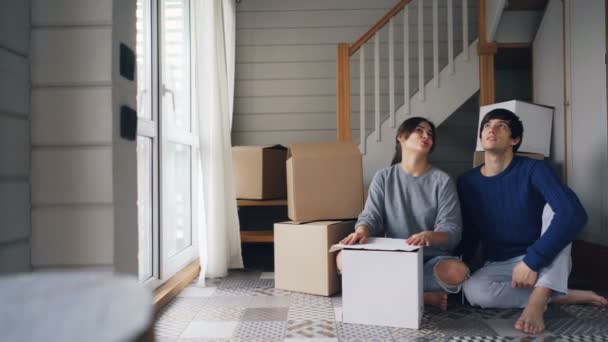 Tipo guapo está hablando con su novia sentada en el piso de la nueva casa y luego besarla y darle las llaves invitando a mudarse. Concepto de reubicación y relación . — Vídeos de Stock