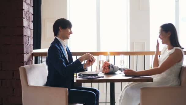 Bella giovane donna è entusiasta di proposta di matrimonio nel ristorante mentre il suo ragazzo sta parlando poi mettendo anello al dito e baciare la mano. Amore e concetto di famiglia . — Video Stock