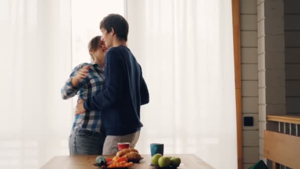 Adorável casal homem e mulher estão dançando e beijando na cozinha em casa vestindo roupas casuais desfrutando de tempo juntos. Concepção de habitação, família e amor . — Vídeo de Stock