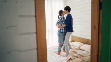 Neşeli genç aşıklar yatakta ev yatak odasında eğleniyor ve dikkatsizce gülüyor, dans ediyorlar. Mutlu gençlik, modern yaşam tarzı ve ilişki kavramı.